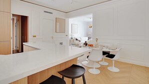 A modern kitchen with a large island, white cabinetry, and a dining area with white chairs and a table. - Elegant A/C Apt 2br/6p - Paris 17th/monceau (Paris)
