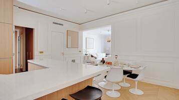 A modern kitchen with a large island, white cabinetry, and a dining area with white chairs and a table.