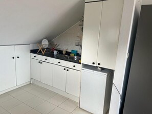 Una cocina compacta con armarios blancos, encimera negra y lavavajillas integrado.