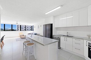 A modern kitchen with white cabinets, a large island, bar stools, and a view of the city. - Modern 2BDR apartment in the heart of Broadbeach (Gold Coast)