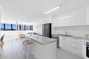 A modern kitchen with white cabinetry, a large island, and a view of a building through the window. - Stylish 2BDR Retreat in Broadbeach Sleeps 4 (Gold Coast)