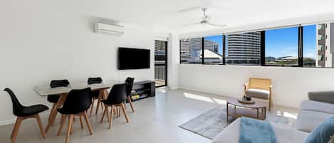 Una sala de estar moderna con comedor, un televisor de pantalla plana en la pared y un ventanal con vistas a la ciudad.
