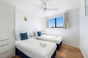 A hotel room with two beds, a ceiling fan, a window with curtains, and a view of the sky. - Stylish 2BDR Retreat in Broadbeach Sleeps 4 (Gold Coast)