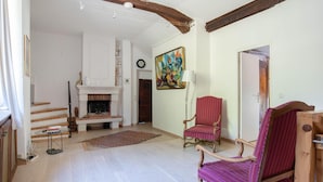 Un salon avec une cheminée, un fauteuil rouge, une table en bois et un tableau accroché au mur.