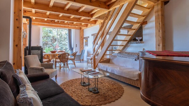 Un salon chaleureux avec un plafond en bois, un canapé, une table basse et un escalier menant à un niveau supérieur.