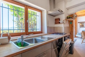 A kitchen with a double sink, wooden cabinets, a stove, and a window with a view of greenery. - Charming Home Near Verdon Gorges & Pool (Digne-les-Bains)