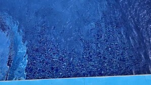Ein rechteckiger Swimmingpool mit blauer Innenauskleidung, umgeben von einer weißen Mauer und einer kleinen Rasenfläche.