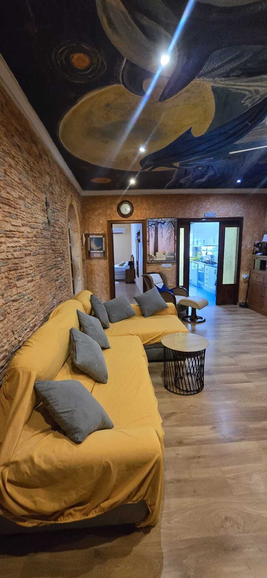 Een kamer met een gele bank, een ronde tafel en een plafond met een drakenmuurdecoratie.