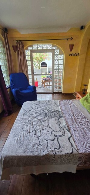 A room with a bed, a blue chair, a window with curtains, and a view of the outside. - Villa Noa. (Torrevieja)