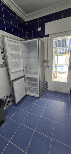 A kitchen with a blue tiled floor, a refrigerator, and a door leading to an outdoor area. - Villa Noa. (Torrevieja)