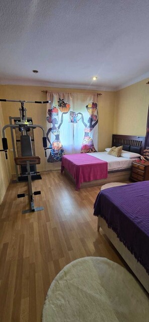 Een slaapkamer met een bed, bureau, stoel, raam met gordijnen en een plafondventilator.