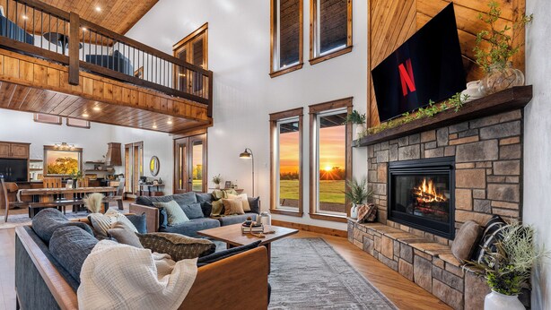 Ein geräumiges Wohnzimmer mit Kamin aus Stein, einem großen Fernseher darüber und einer gemütlichen Sitzecke mit Sofa und Couchtisch.