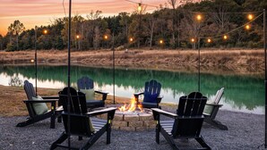 Ein Sitzbereich am Seeufer mit Adirondack-Stühlen und einem Feuerkorb, umgeben von einem Kiesweg und Lichterketten.
