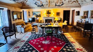 A room with a high ceiling featuring ornate frescoes, a central fireplace, a dining area with a table and chairs, and a patterned rug. - Fabulous farm in Mesquitela, Mangualde for vacation with pool for 18 people (Mesquitela)
