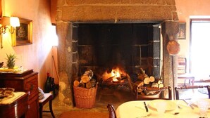 A stone fireplace with logs, a dining table set with plates and cutlery, and a wicker basket of firewood. - Fabulous farm in Mesquitela, Mangualde for vacation with pool for 18 people (Mesquitela)