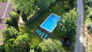 An aerial view of a rectangular swimming pool surrounded by lush greenery, with a stone pathway leading to a row of lounge chairs.