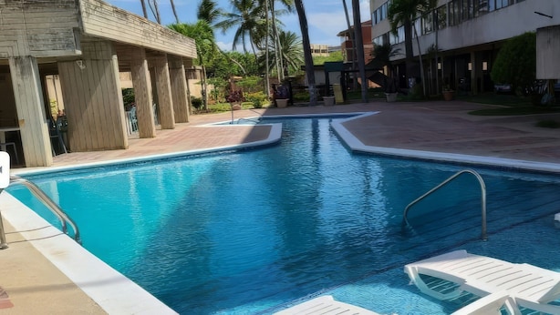 A swimming pool with lounge chairs and a building with a modern design. - Studio in Zona Top, steps from the beach (Near City Place and La Vela) (Pampatar)