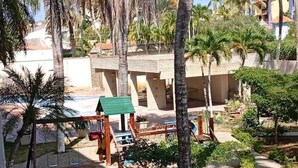 A resort with palm trees, a swing set, and a covered seating area. - Studio in Zona Top, steps from the beach (Near City Place and La Vela) (Pampatar)