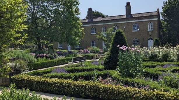 A building with a brick facade and multiple windows, surrounded by a well-maintained garden with various plants and flowers. - Peaceful London City Apartment & Free Parking (London)