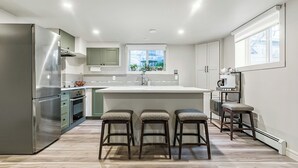 Una cocina moderna con un refrigerador de acero inoxidable, una isla central con taburetes y un ventanal que proporciona luz natural.