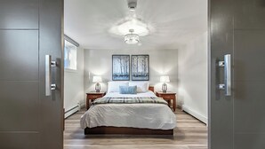 Un dormitorio moderno con una cama grande, dos mesitas de noche con lámparas, una lámpara de techo y dos cuadros enmarcados en la pared.