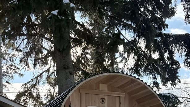 Una estructura de sauna de madera con puerta, un banco y una pequeña mesa.