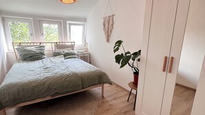 Makuuhuone, jossa on sänky, pyöreä matto, ruukkukasvi, vaatekaappi ja riippuvalaisin.