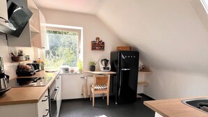 Moderni keittiö, jossa on musta jääkaappi, puinen ruokapöytä ja tuoli sekä ikkuna, josta tulee luonnonvaloa.