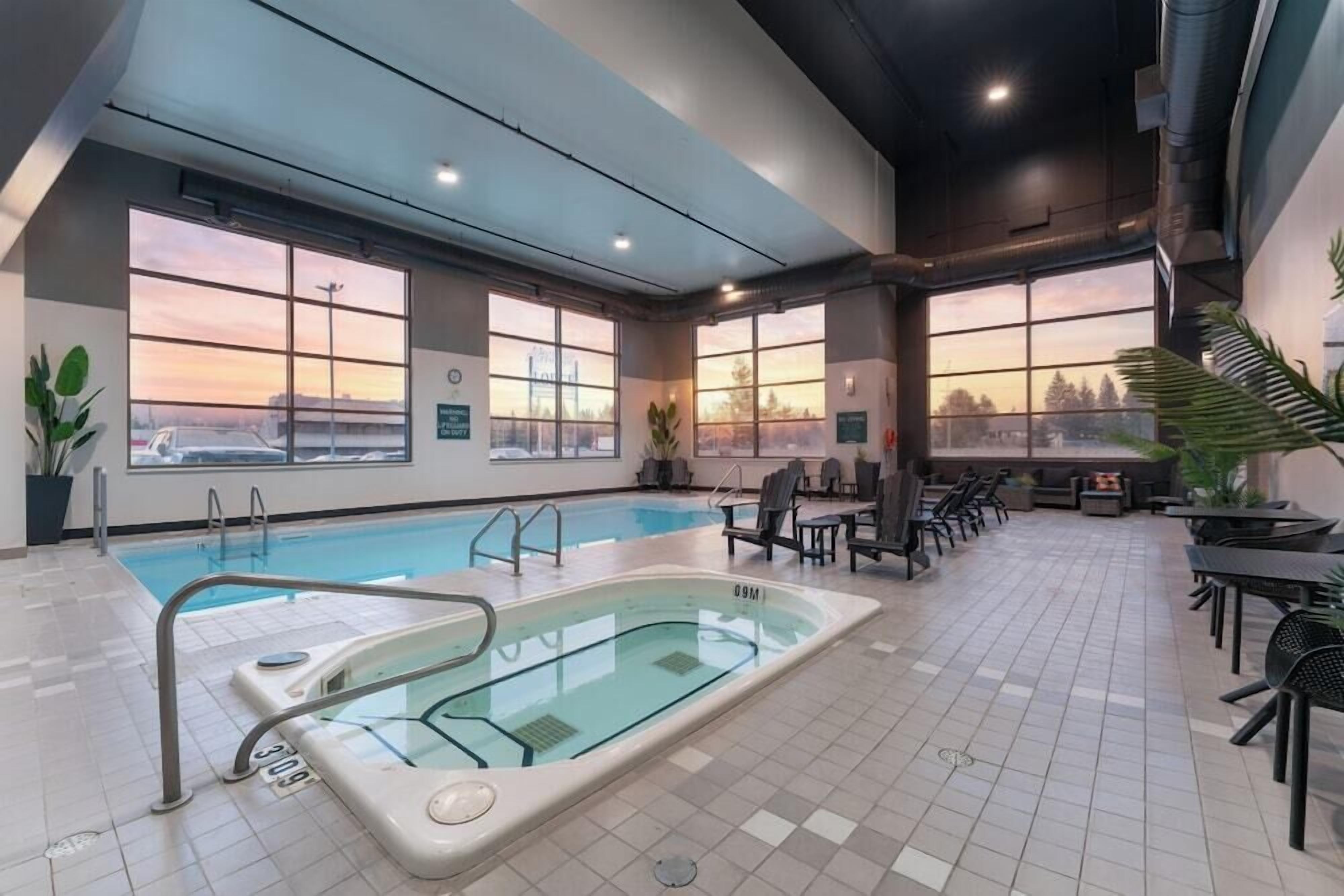 An indoor swimming pool with a view of the sunset, surrounded by seating areas and potted plants.