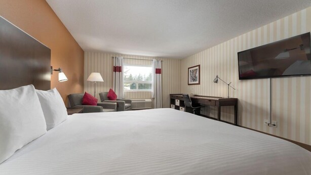 A hotel room with a large bed, a desk, a chair, a TV, and a window with curtains. - Four Points By Sheraton Prince George (Prince George)