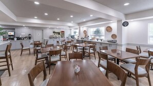 A spacious dining area with multiple tables and chairs, a kitchen in the background, and a sign on the wall. - Four Points By Sheraton Prince George (Prince George)