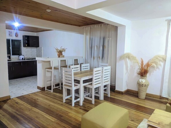 A dining area with a wooden table and chairs, a kitchen in the background, and a decorative vase with pampas grass.