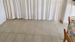 A room with a large window covered by white curtains, a tiled floor, and a wooden chair with a patterned cushion. - House in the Marine di Sant'Ambroggio, 10-minute walk to the sea, large terrace (Lumio)