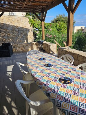 An outdoor patio with a stone wall, a grill, and a table covered with a colorful tablecloth. - House in Marine di Sant'Ambroggio, 10 minutes from the ocean, large terrace (Lumio)