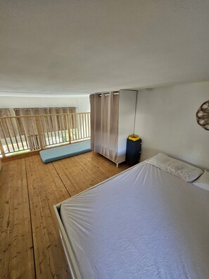 A bedroom with a wooden floor, a bed, a window with curtains, and a balcony with a railing. - House in Marine di Sant'Ambroggio, 10 minutes from the ocean, large terrace (Lumio)