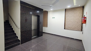 A modern hallway with a marble floor, a staircase, an elevator, a ceiling fan, and a fire extinguisher. - SHIVOM RESIDENCY (Hyderabad)
