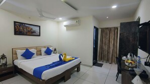 A hotel room with a bed, bedside table, and a desk with a chair. - SHIVOM RESIDENCY (Hyderabad)