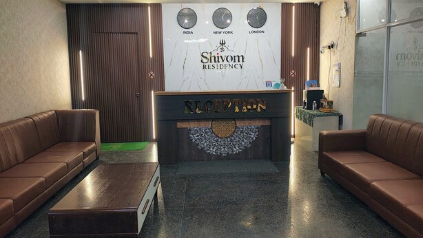 A reception area with a reception desk, two brown leather sofas, a wooden coffee table, and a wall with clocks showing different time zones. - SHIVOM RESIDENCY (Hyderabad)