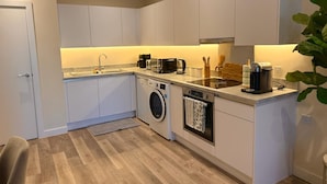 A modern kitchen with white cabinets, a built-in washing machine, a dishwasher, and a coffee maker. - White City Luxury | 1BR Apartment | Prime Location (London)