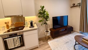 A modern kitchen with a built-in oven, a dining area with a table and chairs, a flat-screen TV, and a potted plant. - White City Luxury | 1BR Apartment | Prime Location (London)
