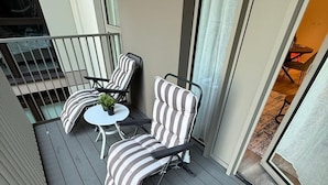 A balcony with two striped cushioned chairs and a small round table, a potted plant, and a view of the interior of the building. - White City Luxury | 1BR Apartment | Prime Location (London)
