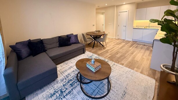 A modern living room with a grey sofa, a round coffee table, and a dining table with chairs. - White City Luxury | 1BR Apartment | Prime Location (London)