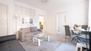 A modern living room with a grey sofa, a glass coffee table, and a dining area with a glass table and chairs. - Central London Apartment St James's Park (London)