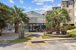 A modern building with a glass entrance, palm trees, and a pool area. - Cozy 2-bedroom condo in quaint Atlantic Beach with private beach access (Atlantic Beach)