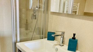 Un baño con lavamanos blanco, un espejo y cabina de ducha.