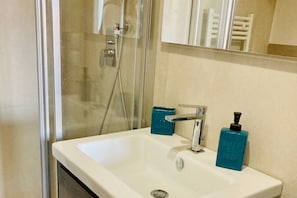Une salle de bain avec un lavabo blanc, un miroir et un espace douche.