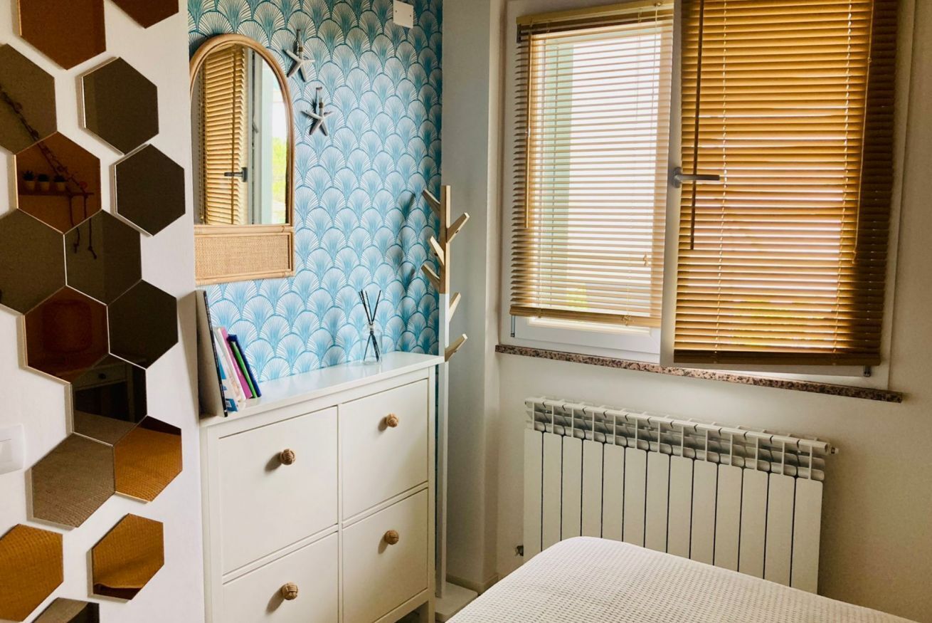 A bedroom with a white dresser, a mirror, a radiator, and a window with blinds.