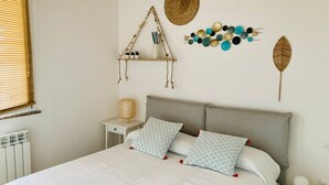 Una cama con almohadas estampadas, una mesita de noche con lámpara, un estante en la pared con plantas y decoración mural.