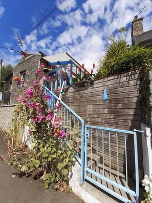 A wooden house with a blue metal staircase leading to a porch. - Colorful little house (Plérin)