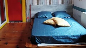 A room with a bed, a red door, and a wooden floor.